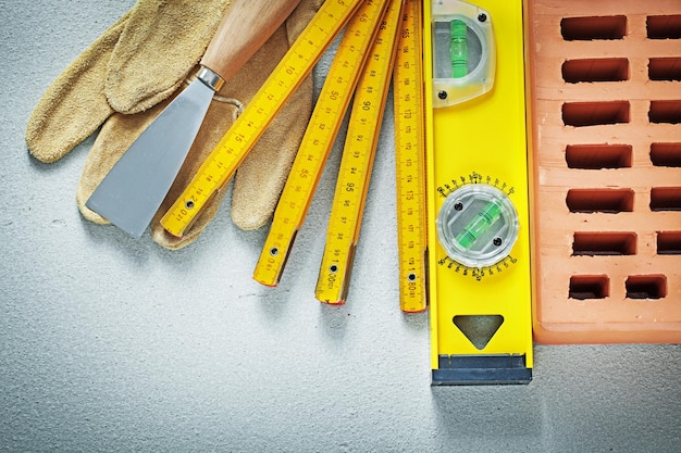 Schutzhandschuhe aus rotem Backstein Spachtel Bauhöhe Holzmeter auf Betonhintergrund Maurerkonzept