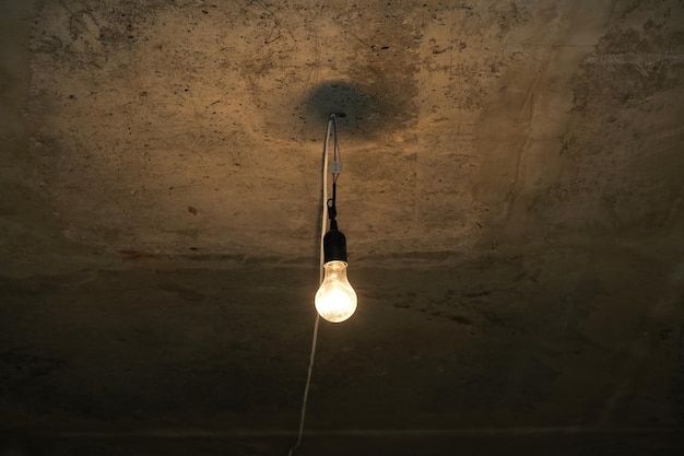 Schwache Glühbirne an der Betondecke des Kellers oder des Luftschutzbunkers. Elektrische Lampe. Temporäre Beleuchtung.