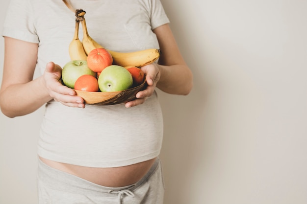 Schwangere Bauch, Frau mit gesundem Essen, Obstschale in Händen. Speicherplatz kopieren.