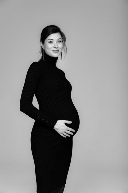 Schwangere Brünette in einem schwarzen Kleid mit Hals auf grauem Hintergrund