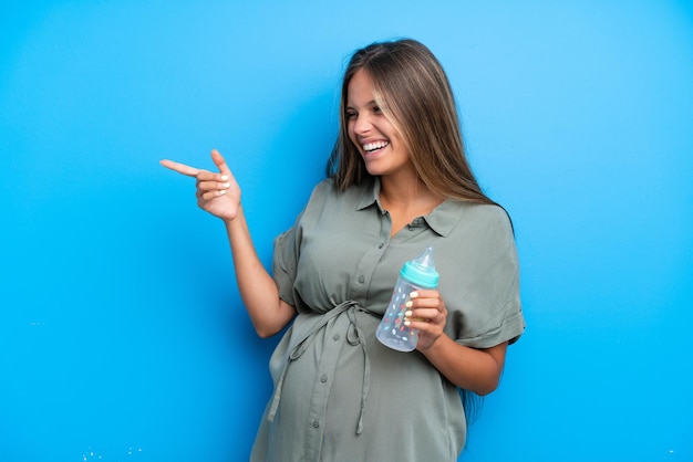 Schwangere Frau auf blauem Hintergrund zeigt mit dem Finger zur Seite und präsentiert ein Produkt