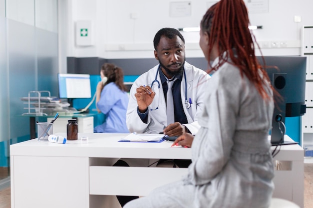 Schwangere Frau beim Kontrolltermin mit Arzt in Arztpraxis. Patientin mit Schwangerschaft, die bei der Konsultation mit dem Hausarzt über Gesundheitsversorgung und Elternschaft spricht