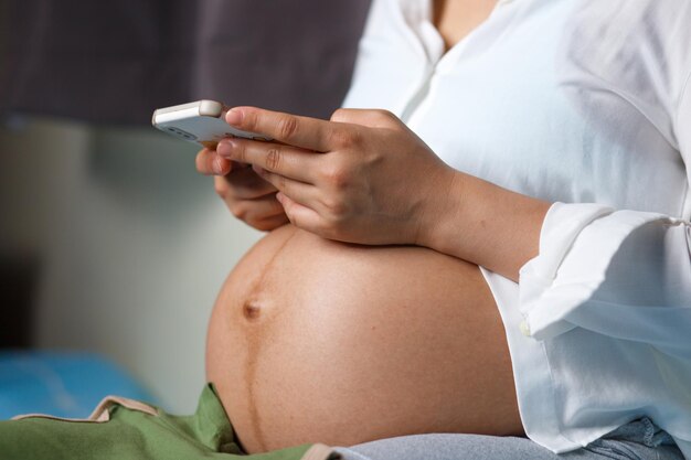 Schwangere Frau benutzt ein Smartphone für eine Nahaufnahme von Bauch und Händen