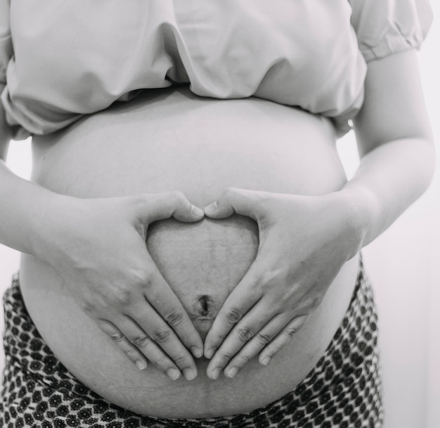 Schwangere Frau des jungen Erwachsenen in der weißen Kleidung, die großen nackten Bauch mit den Händen berührt, die Form zeigen Schwangerschaftskonzept Erwartungszeit Nahaufnahme lokalisiert auf hellgrauem Wandhintergrund