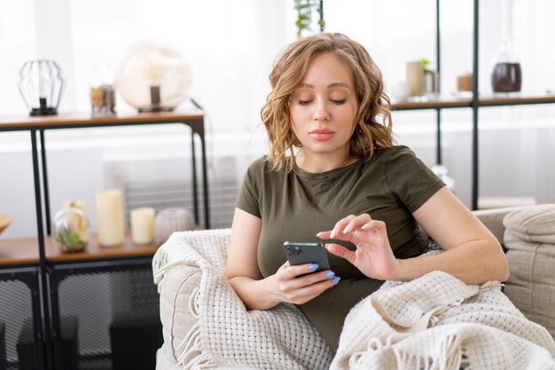 Schwangere Frau, die auf der Couch liegt und Smartphone in der Hand hält Entspannen Sie sich, genießen Sie Atmosphäre