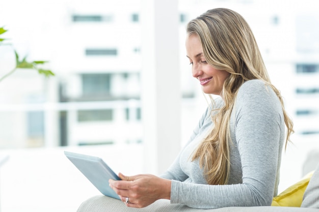 Schwangere Frau, die auf Sofa sitzt und digitale Tablette verwendet