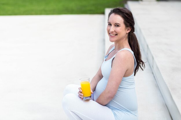Schwangere Frau, die auf Treppen sitzt und Orangensaft trinkt