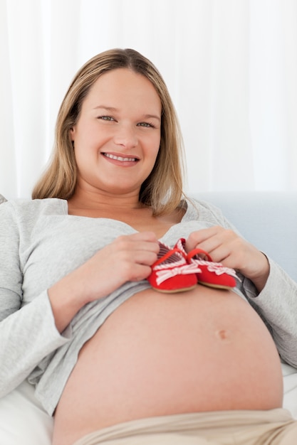 Schwangere Frau, die Babyschuhe auf ihren Bauch setzt