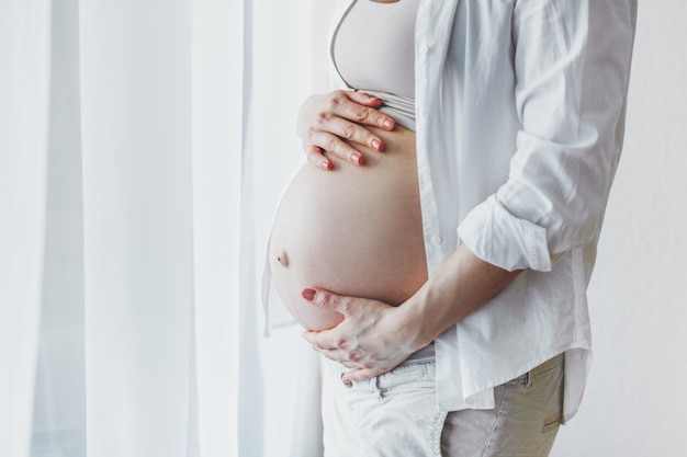 Schwangere Frau, die Bauch berührt, der zu Hause Schwangerschaft genießt. Lebensstil