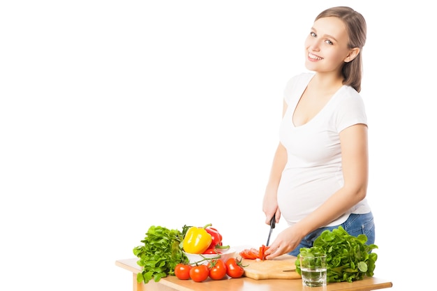 Schwangere Frau, die beim Schneiden von Gemüse in die Kamera schaut