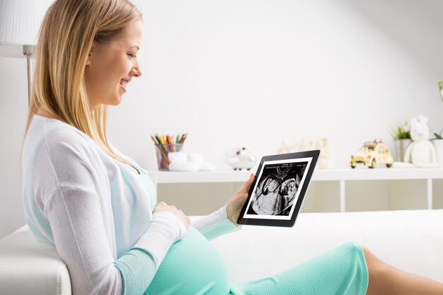 Schwangere Frau, die ein Tablet verwendet, um sich die Ergebnisse der Sonographie anzusehen