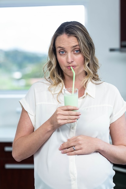 Schwangere Frau, die einen Smoothie in der Küche trinkt