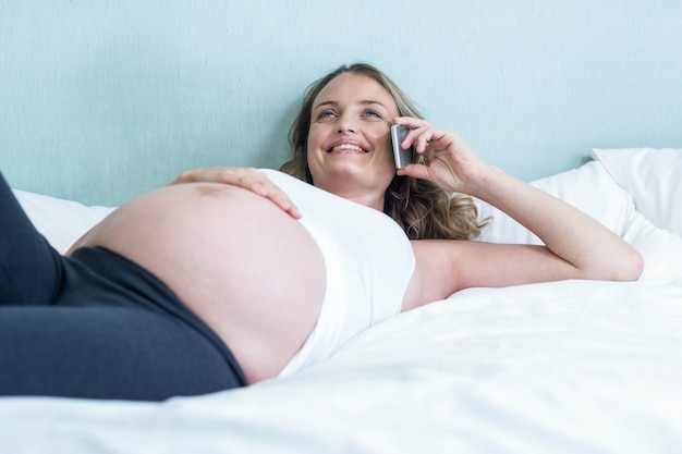 Schwangere frau, die einen telefonanruf auf ihrem bett macht