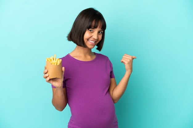 Schwangere Frau, die gebratene Chips über isoliertem Hintergrund hält und auf die Seite zeigt, um ein Produkt zu präsentieren