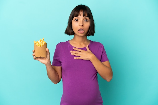 Schwangere Frau, die gebratene Chips über isolierter Oberfläche hält, überrascht und schockiert, während sie nach rechts schaut