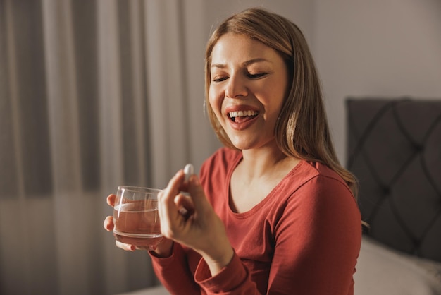 Schwangere Frau, die Glas mit Wasser hält und zu Hause pränatale Vitaminpille trinkt.