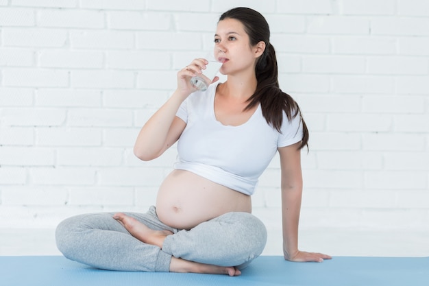 Schwangere Frau, die Glas Wasser nach Yoga oder pilates hält