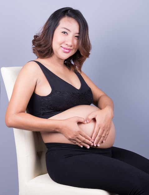 Schwangere Frau, die ihre Hände in einer Herzform auf Bauch hält