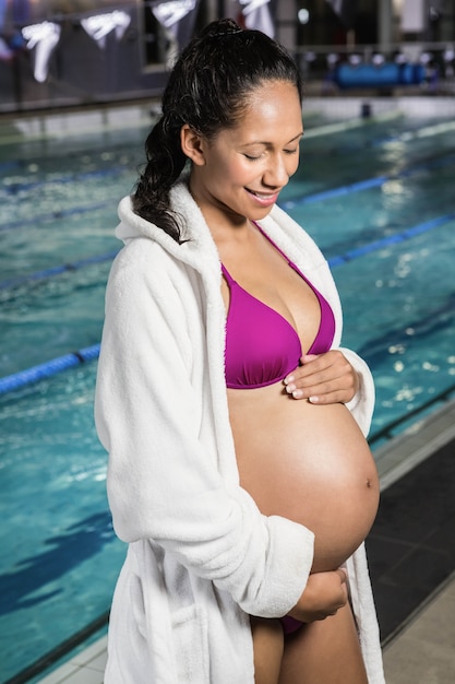 Schwangere Frau, die ihren Bauch am Swimmingpool berührt