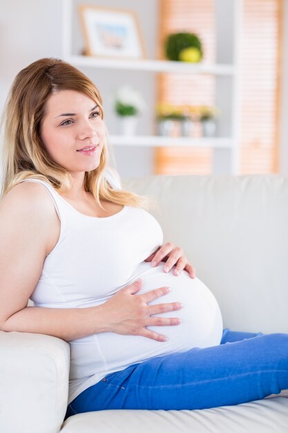 Schwangere Frau, die ihren Bauch auf der Couch berührt