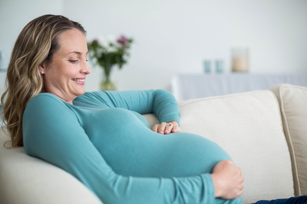 Schwangere Frau, die ihren Bauch liegt auf der Couch berührt