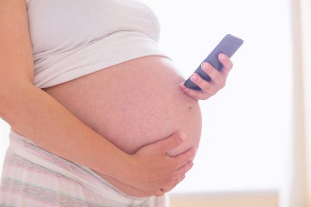 Schwangere Frau, die ihren Smartphone verwendet