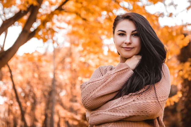 Schwangere Frau, die im herbstlichen Stadtparkwald steht, gekleideter warmer Wollpullover