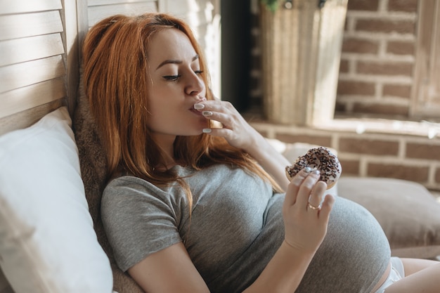 Schwangere Frau, die leckere Donuts isst
