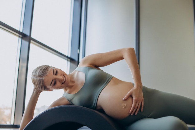 Schwangere Frau, die mit Hilfe des Reformers im Pilates-Kurs trainiert