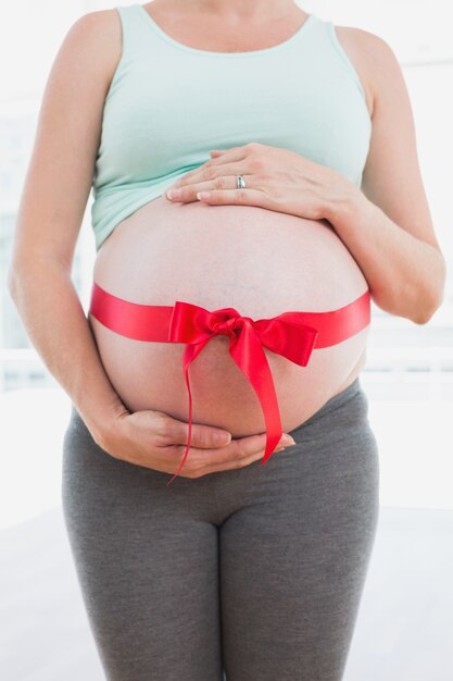 Schwangere Frau, die mit rotem Bogen um Bauch steht