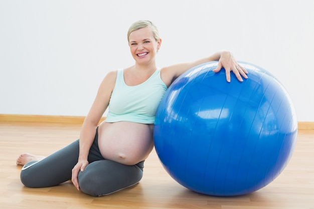 Schwangere Frau, die neben dem Übungsball lächelt an der Kamera sitzt