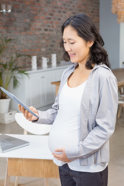 Schwangere Frau, die Tablette im Wohnzimmer verwendet