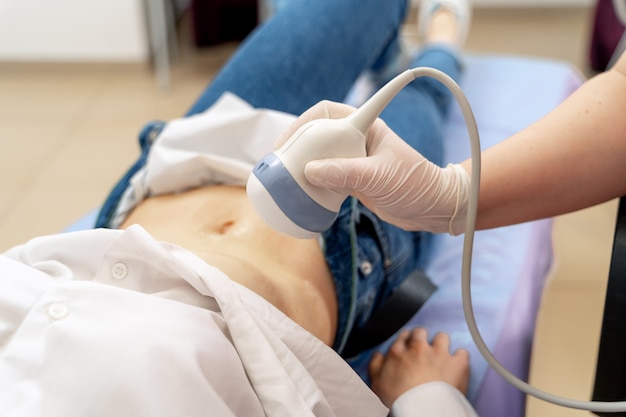 Schwangere Frau, die Ultraschall vom Arzt bekommt. Ultraschallgeräte in der Klinik. Selektiver Fokus auf Bauch.