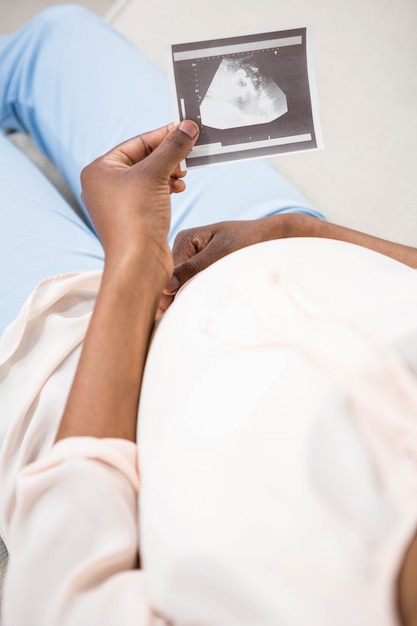 Schwangere frau, die ultraschallscan auf couch hält