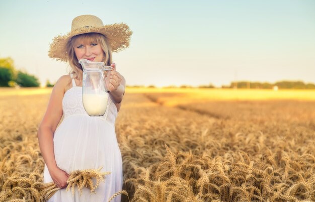 Schwangere Frau, die weißes Kleid trägt und Krug Milch in einem Weizenfeld hält