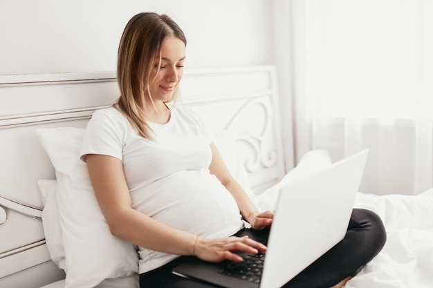 Schwangere Frau, die zu Hause an Laptop arbeitet