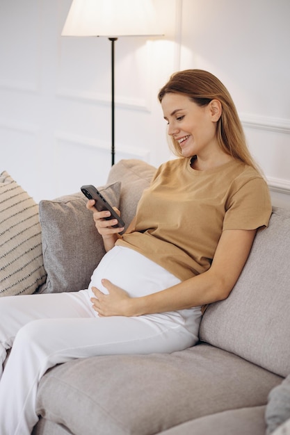 Schwangere Frau, die zu Hause auf dem Sofa sitzt und telefoniert