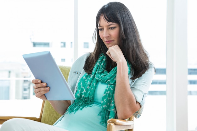 Schwangere Frau, die zu Hause digitale Tablette verwendet