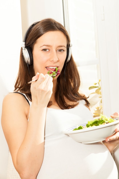 Schwangere Frau essen Salat und hören Musik