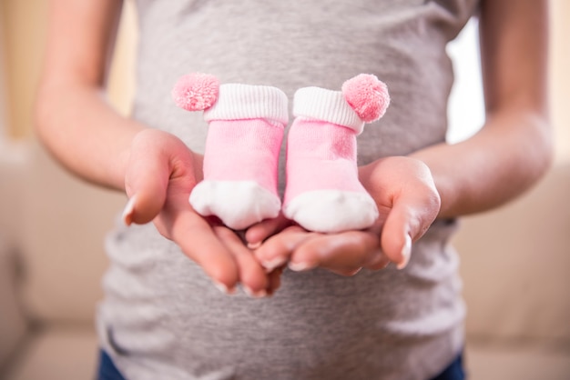 Schwangere Frau hält Bauch auf kleinen Socken für Babys.