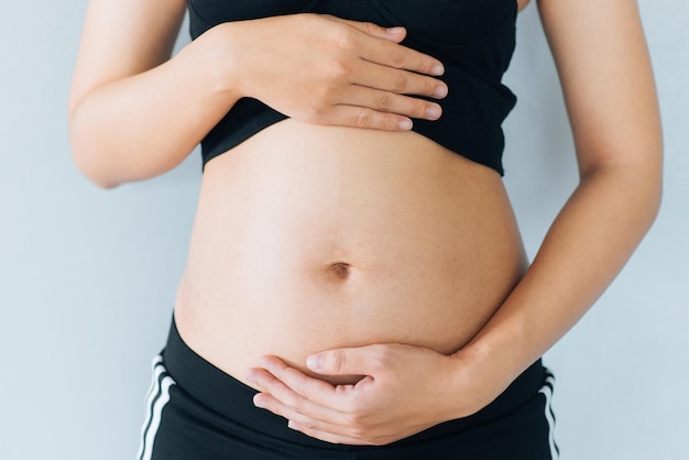 Schwangere Frau hält die Hände auf Bauch und pastellfarbenem Hintergrund Schwangerschaft Mutterschaft Vorbereitung und Erwartung Konzept Closeup Kopie Raum Junge Frau wartet auf die Geburt eines Babys