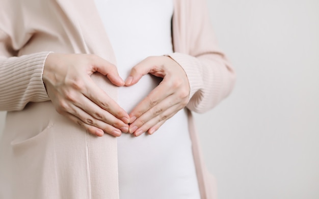 Schwangere Frau hält die Hände auf dem Bauch auf einem weißen Hintergrund Schwangerschaftsvorbereitungs- und Erwartungskonzept