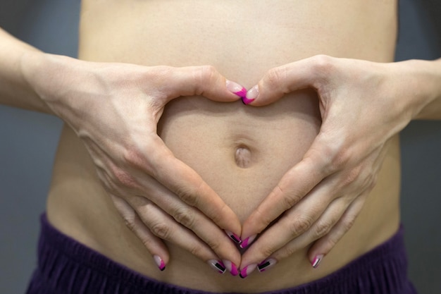 Schwangere Frau hält ihre Hände in Form eines Herzens auf ihrem Bauch, Nahaufnahme. Herzförmige Hände