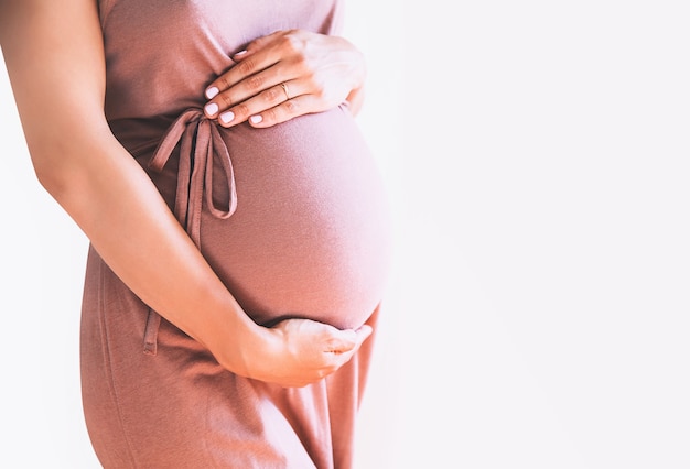 Schwangere Frau im Kleid hält die Hände auf dem Bauch auf weißem Hintergrund