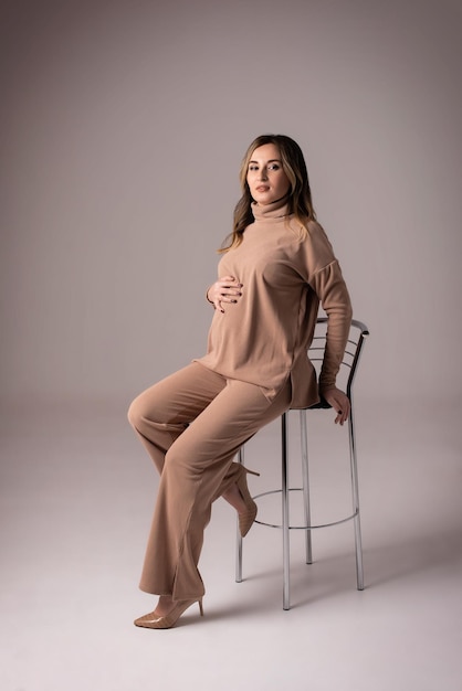 Schwangere Frau in einem beigen Anzug auf grauem Hintergrund Stilvolle Schwangerschaft