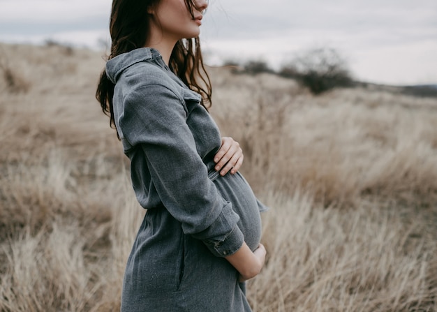 Schwangere Frau in einem Feld am kalten Herbsttag