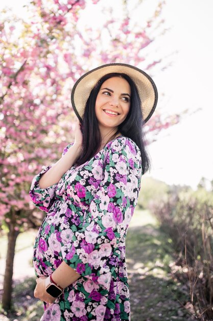 Schwangere Frau in einem Kleid mit schwarzen Haaren in der Nähe von Kirschblüten im Frühjahr