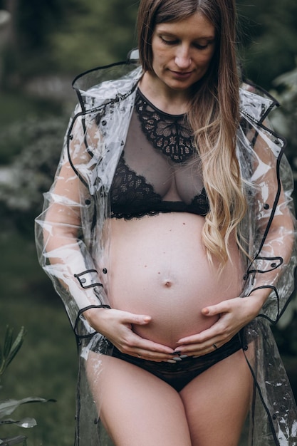 schwangere Frau in einem Regenmantel im Park