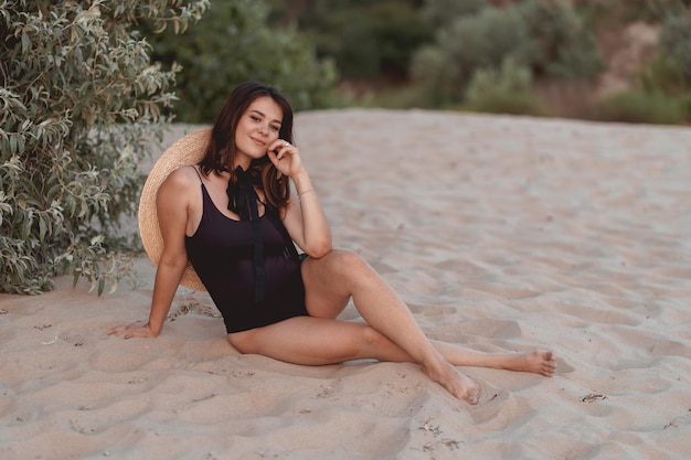 Schwangere Frau in einem schwarzen Badeanzug und Hut an einem Sandstrand