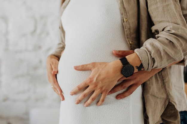 Schwangere Frau in einem weißen Kleid mit ihrem Mann in einem Wohnzimmer